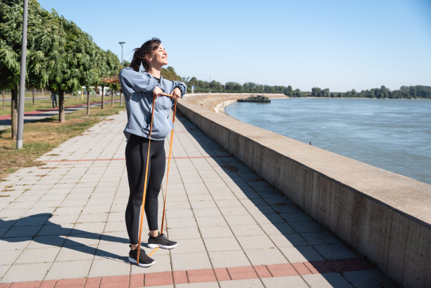 年轻美丽快乐的运动女性训练与阻力橡胶的灵活性和肌肉激活。活跃的职场女性早上去办公室上班之前会进行户外锻炼。图片下载