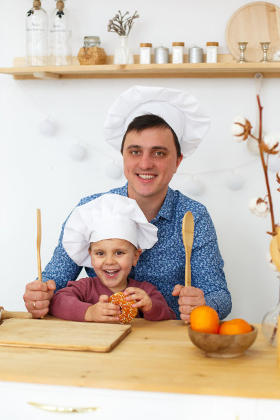 父亲和他戴着厨师帽子的小儿子在厨房里图片下载