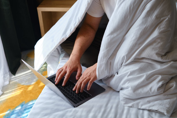 一个商人在床上的笔记本电脑上通过程序和应用程序来进行谈判。用笔记本电脑工作。经营理念。在家工作的自由职业者。在线交流图片下载