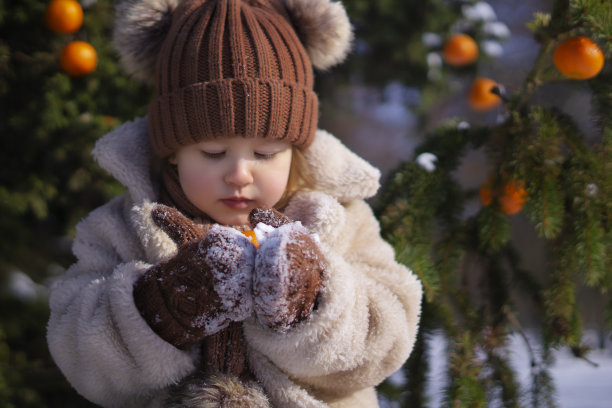 可爱的小女孩在冬天的一天，在公园里享受时光，采摘橘子。库存图片图片下载