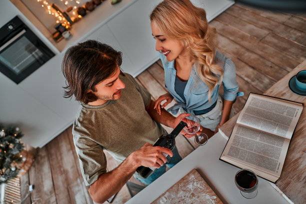 英俊的男人在厨房里给妻子倒红酒。俯视图图片下载