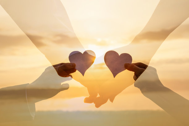 在阳光明媚的夕阳下，情侣们伸出纸上的心。图片下载