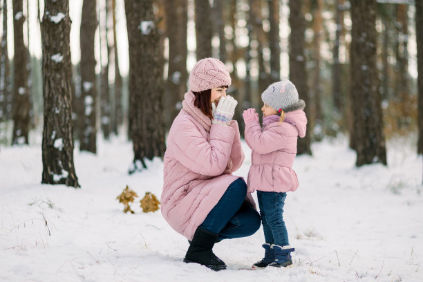 冬天，妈妈和她可爱的小女儿在白雪皑皑的森林里散步。妈妈和孩子穿着粉红色的夹克，带着爱和温柔看着对方。图片下载