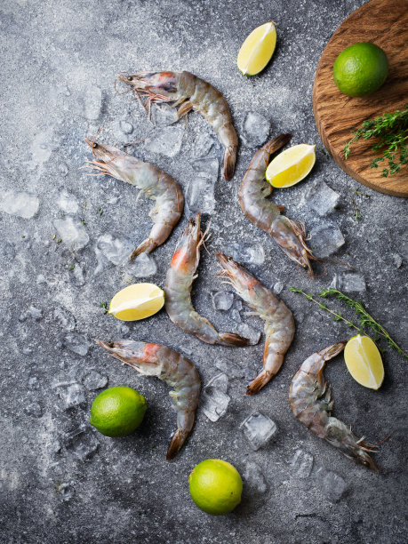 灰色背景上的虎虾和冰。深色的桌子上放着生海鲜。鲜虾、酸橙和百里香图片下载