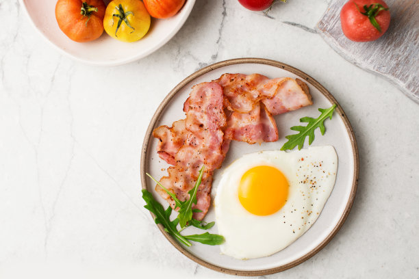 英式早餐。鸡蛋和煎培根。一个装有西红柿的杯子。在大理石桌子上端早餐。煎蛋。图片下载