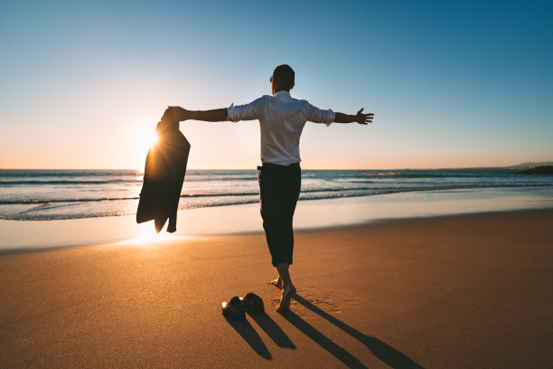 生活是美好的。男人张开双臂，在日落的沙滩上享受生活和自由图片下载