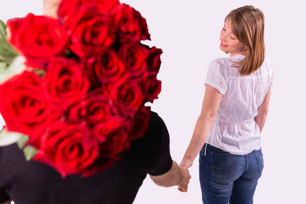 后视图照片，一个金发女人越过她的肩膀，握着送货员的手，他把一大束玫瑰放在他的肩膀上。图片下载