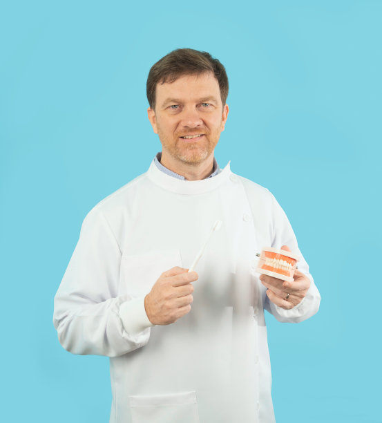 在医院诊所，快乐的白人牙医的肖像，人们微笑着，拿着假牙和牙刷。医生被隔离在蓝色。牙医。医疗和牙科保健。图片下载