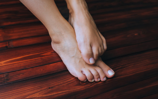 两个女性的脚在一个棕色木地板背景近。有真菌的瘙痒和抓挠。足部卫生的概念。图片下载