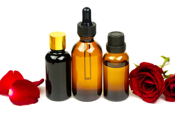 玫瑰油玻璃瓶与红色玫瑰花孤立在白色的背景。图片下载
