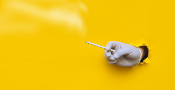 医生(护士)戴着白色保护性医用手套，手里拿着一支细烟。黄色的纸上有个破洞。covid-19期间卫生工作者的吸烟观念和习惯控制图片下载