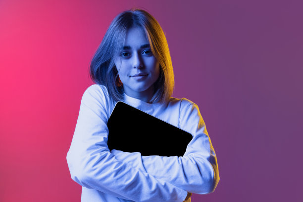 年轻女孩、青少年或学生的肖像，穿着白色休闲装，在霓虹灯下用平板电脑、小玩意隔离在粉紫色渐变背景下图片下载