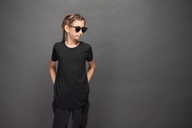 小女孩穿着黑色t恤与空间为您的标志或设计在工作室的灰色背景图片下载