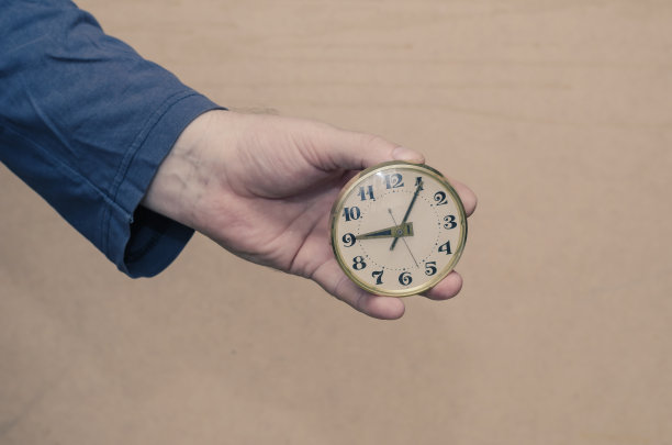 成年男性手持一个圆形时钟在他的手对着棕色的bac图片下载