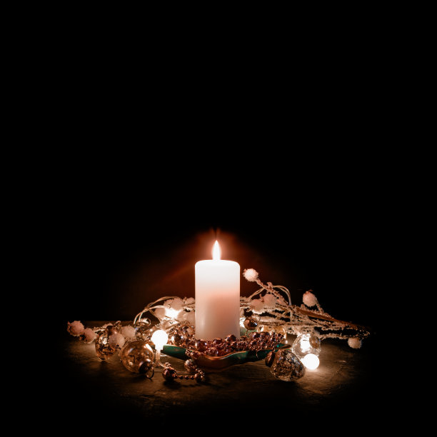 一根燃烧的蜡烛在大浅盘上。旁边是一个发光的花环，树枝上挂着浆果和珠子。简单的圣诞节的概念。黑色背景。副本的空间。图片下载