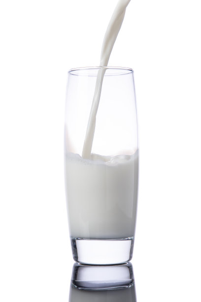把牛奶倒进玻璃杯，放在白色背景上图片下载