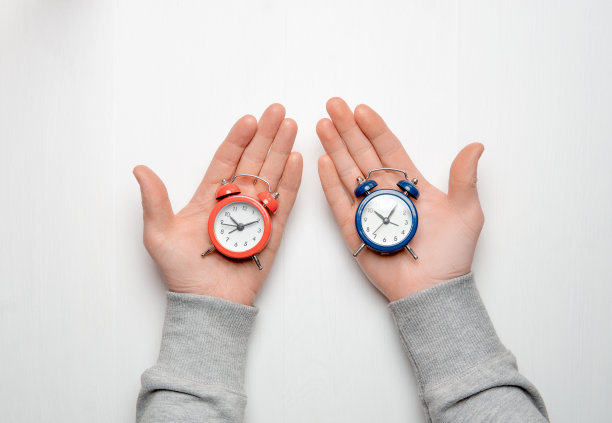 一个男人手里拿着一块表。手里拿着红色和蓝色的闹钟。选择的概念。图片下载