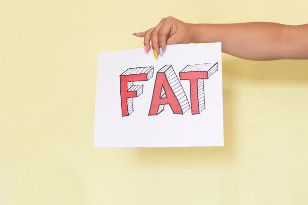 拉丁妇女的手拿着一个标志，黄色背景上有“FAT”字样，模特无法辨认。图片下载