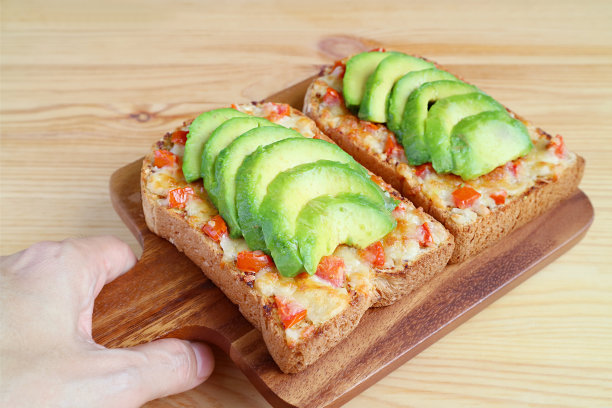 手拿烤奶酪吐司面包板，上面有番茄和牛油果片图片下载