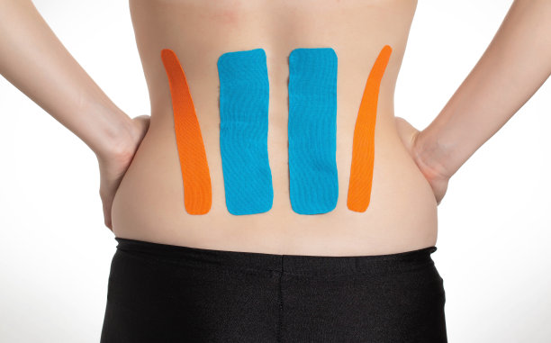 在女孩腰椎的背部贴上橙色和蓝色的运动胶带。胶带问题区域和疼痛缓解图片下载