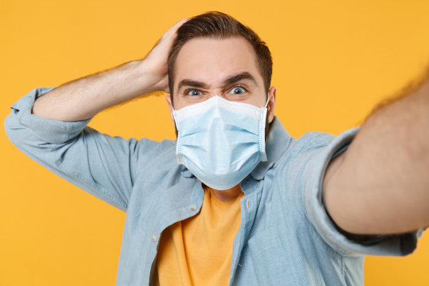 图为戴着无菌口罩的困惑男子被隔离在黄色背景上。流行性大流行冠状病毒2019-ncov sars covid-19流感病毒概念。手放在头上用手机自拍。图片下载