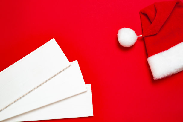 三根白色的木板和红色背景上的圣诞老人帽子。横幅与圣诞节或新年的心情与一个免费的地方为硬件商店或艺术商店或名片的文本图片下载