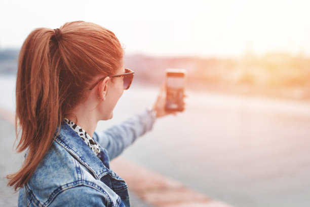 年轻的红发女子拍摄的城市全景智能手机，在日落图片下载