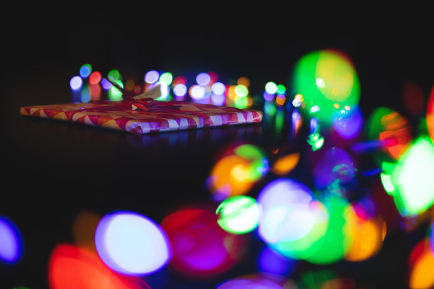 黑色无焦点风格摄影的礼物在节日的圣诞小盒子与丝带在桌子上，与前景和背景抽象节日散景光从花环彩灯图片下载