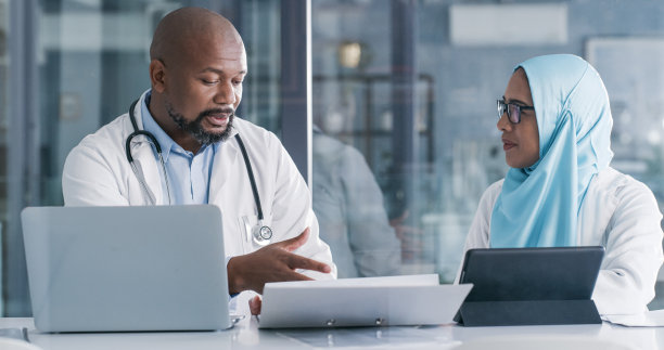 照片中，两名医疗专业人员一边处理文书工作，一边使用科技产品图片下载