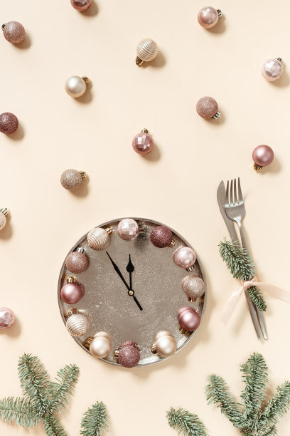 冬季节日餐桌设置概念，圣诞盘与时钟指针显示十二或午夜，闪耀的球米黄色的颜色，刀，叉，杉树树枝。新年假日饮食概念图片下载