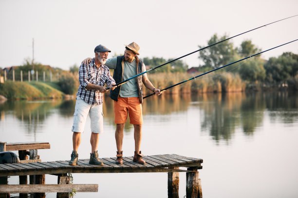 一个快乐的成熟男人和他的儿子在码头钓鱼。图片下载