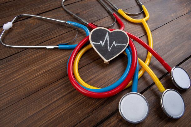 医生的工作场所。彩色听诊器和木桌背景上的小心脏——保健概念图片下载