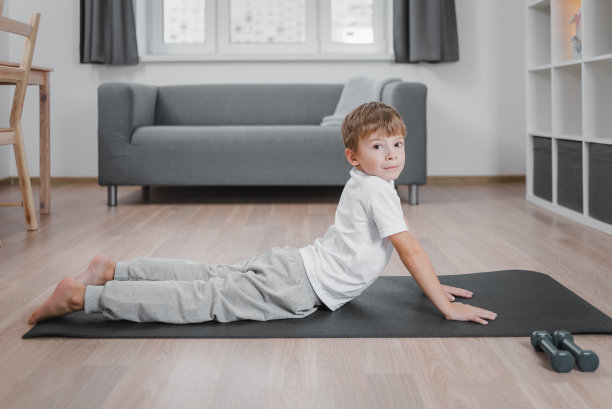 男孩的肖像练习瑜伽，站在向上的狗运动，穿着家里的衣服，在室内全身，看着相机。图片下载