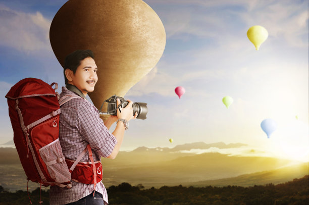亚洲男子背着背包，拿着相机，看着五颜六色的热气球在空中飞行图片下载