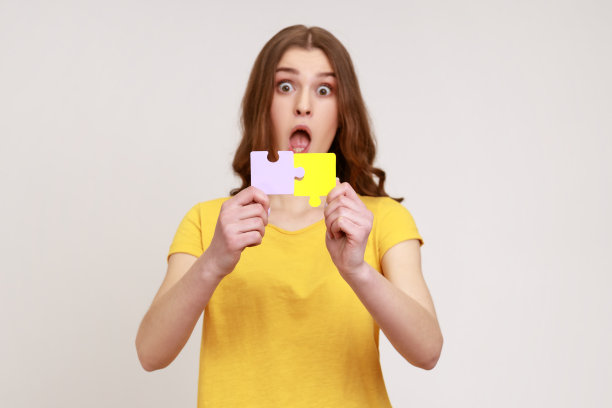 年轻的棕色头发惊讶的女人的肖像，拿着五颜六色的拼图，一个两部分，象征着联系和结合。图片下载