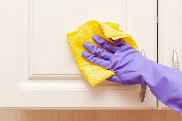 女性手戴紫色橡胶手套擦拭米色的橱柜门。黄布在手图片下载