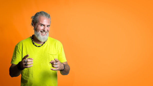 嬉皮士男在镜头前指指点点，留着胡子的男人，灰色头发，橙色背景，复制空间图片下载