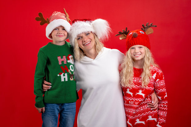 圣诞假期，画一个幸福的三口之家，戴着圣诞帽，妈妈和孩子站在红色的摄影棚背景上微笑图片下载
