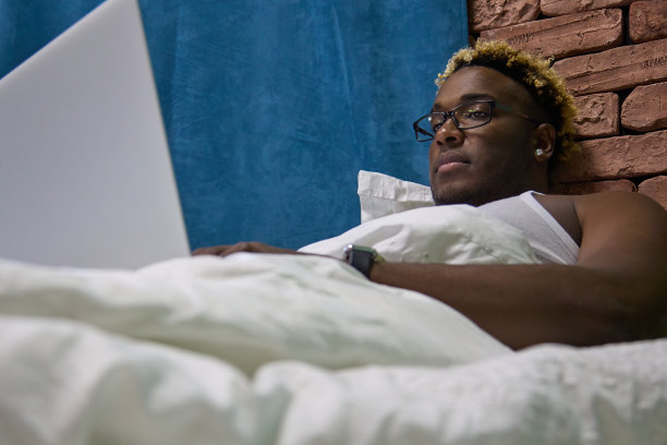 一个黑人在床上用笔记本电脑工作图片下载