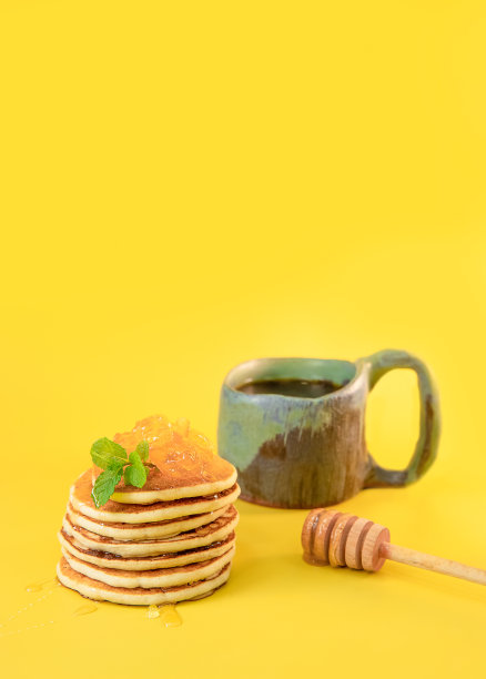 在明亮的黄色背景下，一堆新鲜自制的煎饼和一杯茶，传统的美国早餐，摄影图片下载