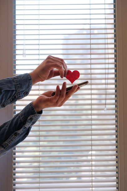 男子手握手机和红心标志靠窗图片下载