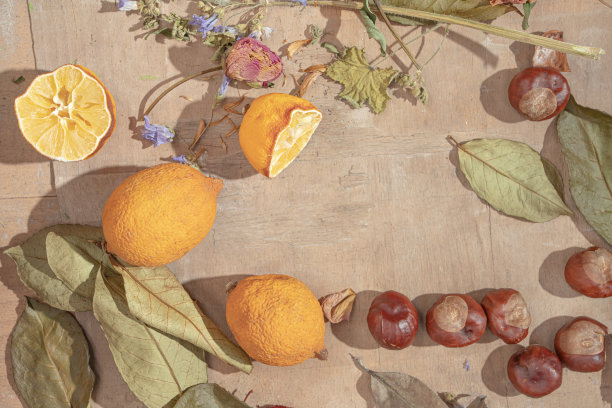 干树叶、花、挤过的柠檬和栗子放在一张简陋的旧木桌上。有空地的平铺布置。秋冬季节概念。图片下载