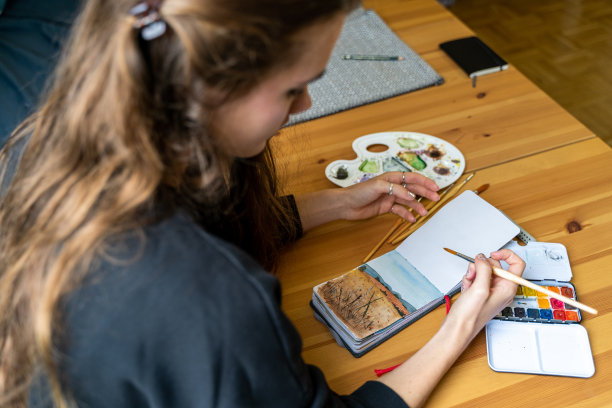 深色皮肤的女人用水彩在纸笔记本上画自然风景图片下载
