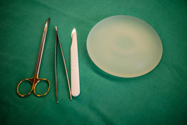 手术剪刀、镊子、手术刀和硅胶乳房植入物放在手术台上。图片下载