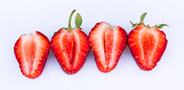新鲜的草莓片。一组四颗草莓切片在白色背景上用绿色叶子排成一行图片下载