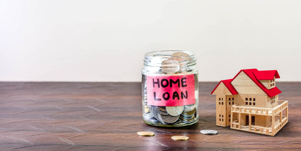 桌上放着一个装满硬币的玻璃瓶。住房贷款就贴在罐子上。概念的形象。图片下载