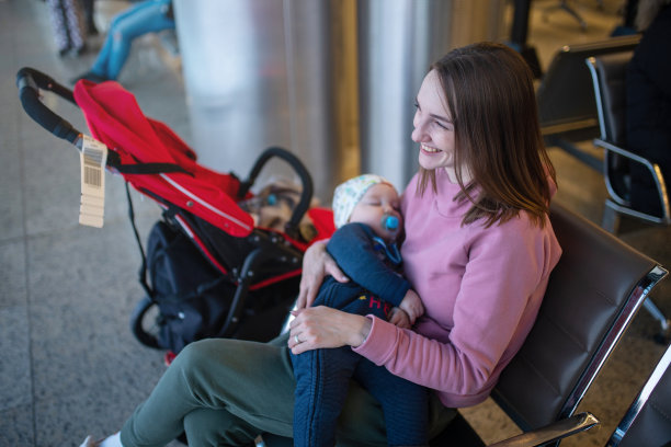 一个微笑的女人抱着一个熟睡的婴儿在机场休息室图片下载