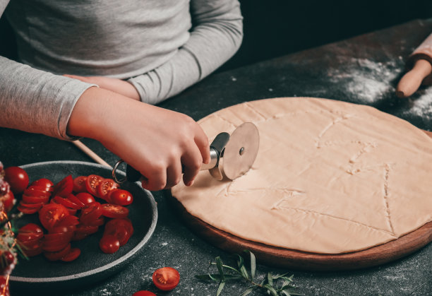 一个白人小女孩的手用一把圆刀切圣诞树——切菜板上的披萨面团像月亮一样薄图片下载