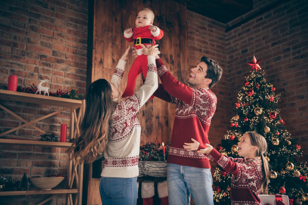 高兴的人们的照片，妈妈，爸爸抱着小男孩，举起手，穿着毛衣在装饰圣诞节的家室内图片下载