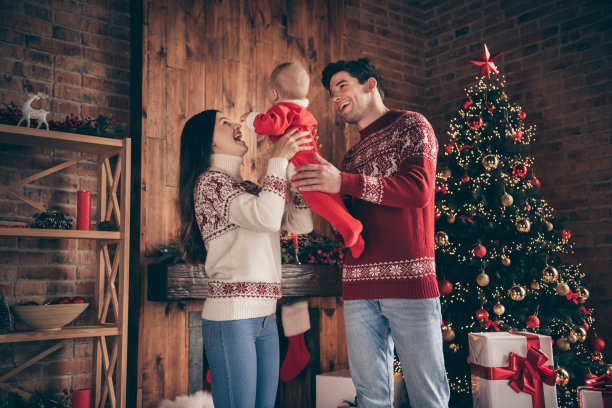照片中，家庭的父母抱着可爱的小男孩，穿着毛衣在装饰过的圣诞节室内图片下载